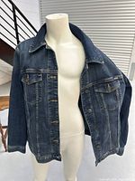 Front and side view of the blue denim-style jacket on a mannequin showing button closure and flap pockets.