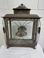 Front view of the large vintage metal lantern candle lamp, showing glass panels and decorative metal floral design on front.