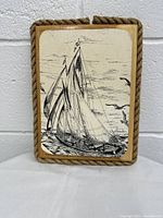 Front view of the monochrome painting showing the sailing ship and rope frame around the wooden board.