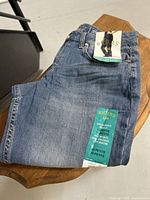 Folded blue denim jeans with attached tags showing brand Riders by Lee and size information 10 Petite.