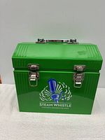 Closed green metal lunch box with Steam Whistle branding on front, metal clasps and handle on top.