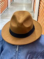 Front view of a brown polyester fedora hat with a black ribbon band, showing its overall shape and condition.