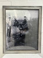 Front view of framed vintage black and white photograph showing two people and a horse outdoors, with wooden frame and glass