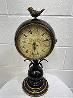 Front view of the vintage double-sided battery-powered clock with bird figurine on top, showing one clock face with Roman numerals and map design.
