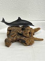 Gray dolphin sculpture resting on a natural wood base with intricate texture and coloration.
