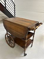 Right-front angled view showing the cart's top, two lower shelves, large wooden spoke wheels on the left, small front caster wheels, and handlebar.