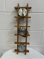 Overall view of the wooden frame holding three instruments vertically: barometer on top, thermometer in the middle, and hygrometer at the bottom.