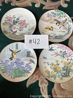 Four decorative plates with Asian bird and floral themes arranged to show front designs, gold trimmed edges visible.