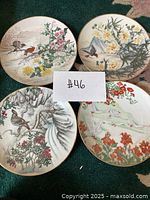 Four decorative Asian-style plates laid out together on carpet, showing bird and floral scenes with gold rims