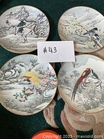 Four Asian bird-themed decorative plates arranged together showing detailed winter landscape and floral designs with gold trimmed edges.