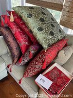 Stack of seven Asian themed decorative throw pillows on a beige sofa showing varied colors and tassels on corners.