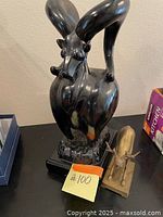 Photo showing the full ceramic ram sculpture and brass deer figurine side by side on a black surface with a lot number in front.