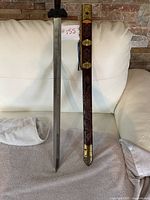 Full view of the sword and sheath placed vertically on a towel against a white couch with a stone wall background.