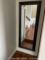 Full view of the full length mirror mounted on a wall with a dark wood frame and gold beaded trim reflecting room and stairs.