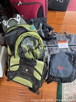 Five assorted bags: a large red wheeled luggage, green and black backpack, gray duffel bag, black and green messenger bag, and a gray and red backpack with TIME branding.