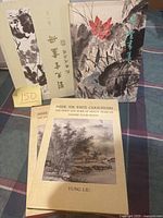 Three hardcover Asian art books shown, including one with a protective slipcase and floral brush painting, and one titled 'Inside the White Cloud Studio' by Yung Liu with a landscape painting on the cover.