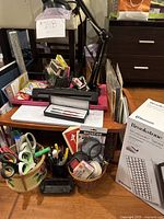 Wide angle photo showing a collection of various home office items including pens, scissors, magnifier, tape dispenser, desk lamp, and folders