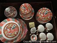 Top view of entire dish set on table, showing stacked plates, cups and bowls with vibrant red, green, and gold phoenix designs.