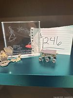 Photo showing the etched JPL paperweight alongside two small rover toys on a dark surface