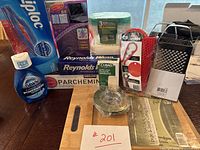 A collection of assorted kitchen products on a dark wood table including Dawn Platinum Powerwash refill bottle, Reynolds aluminum foil, parchment paper, Ziploc gallon size freezer bags, metal grater, jar opener and bamboo chopsticks.