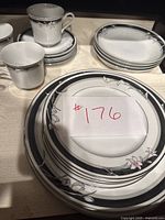 Overall view of stacked dishes showing dinner plates, salad plates, bowls, and tea cups with saucers. White ceramic with floral border in black, grey and pink.