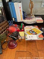 Office and art supplies on desk including binders, books, scissors, paper packs, and small desk lamp