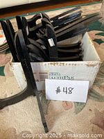 Box containing multiple black wooden stands for displaying plates or picture frames, viewed from side angle showing detail and quantity.