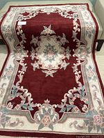 Full view of the burgundy plush area rug with floral medallion and border design in cream and sage green.