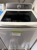 Front view of the Samsung washing machine showing white body and dark glass top lid with control panel.