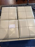 Top view of the cream colored ottoman showing four square stitched sections that are the reversible top quarters.