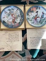 Two decorative Asian plates with traditional artwork and accompanying Chinese text papers.