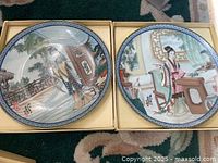 Two Asian decorative porcelain plates side by side in display boxes