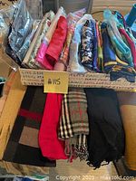 Box containing folded scarves with a note #115. Shows a mix of thick winter scarves and silk-like scarves in various colors and patterns.