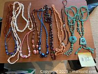 A flat lay of nine women's costume beaded necklaces in shades of peach, brown, blue, and turquoise on a wooden table.
