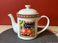 Side view of the ceramic teapot showing the main apple design and decorative border on the lid and body.