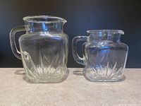 Photo showing the two clear square glass pitchers with starburst pressed design and handles, front view