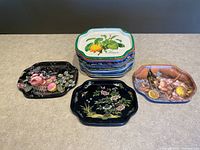 Wide view showing grouped vintage tin snack trays with various colorful designs including fruit and floral prints, stacked and laid out on a table.