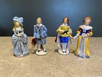 Four porcelain figurines from Occupied Japan era shown side by side on a stone surface against dark background.