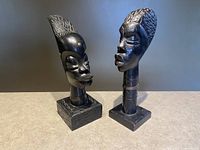 Both hand carved wooden African tribal woman bust sculptures side by side on a flat surface