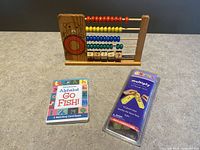 Wooden abacus, Alphabet Go Fish card game, and Multiply math tiles on grey surface