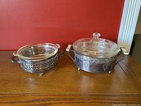 Small and large Pyrex glass serving dishes with silver plate holders on wooden surface against red wall