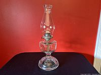 Full view of antique kerosene oil lamp with glass chimney and metal burner on a red background.