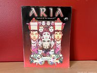 Front cover of the ARIA Canticle of the Monomyth roleplaying game book showing colorful artwork with faces and horned character, red background