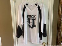 Front view of white Puck U hockey jersey with black accents, showing logo on chest.