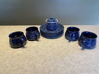 Five blue and white speckled stoneware plates stacked with four matching mugs arranged around them.