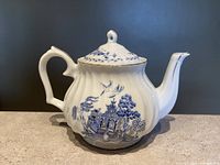 Front-side view of Blue Willow porcelain teapot with blue pattern and gold trim on handle, rim, and spout. Shows overall shape and decoration.
