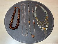 Four necklaces on a round black mat showing amber beads, seed beads, earth-toned beads, and multi-strand colorful statement necklace