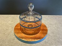 Round wooden cheese board with a clear glass cloche on top, blue painted sides and engraved text visible on board edge