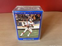 Front view of the Doug Flutie rookie card visible through clear plastic case with blue border, showing Doug Flutie in football gear holding ball on field.