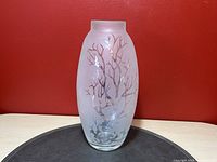 Front view of frosted glass vase showing the matte etched leafless tree design against a red background, placed on an oval black mat.